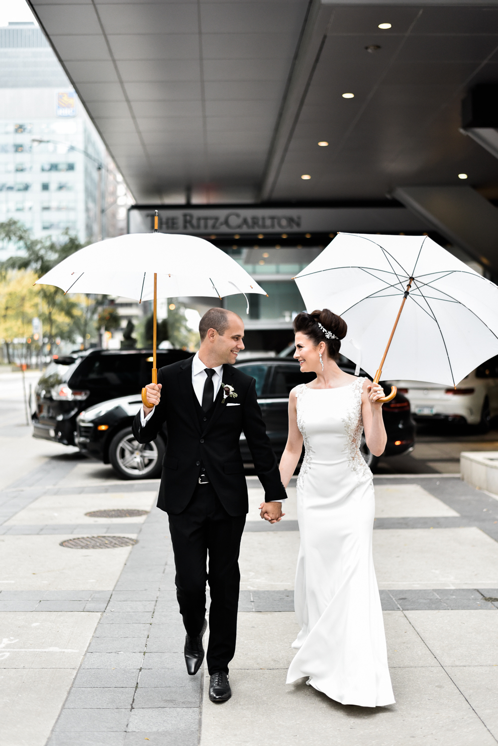 Bride and groom pose with umbrellas outside the Ritz Toronto