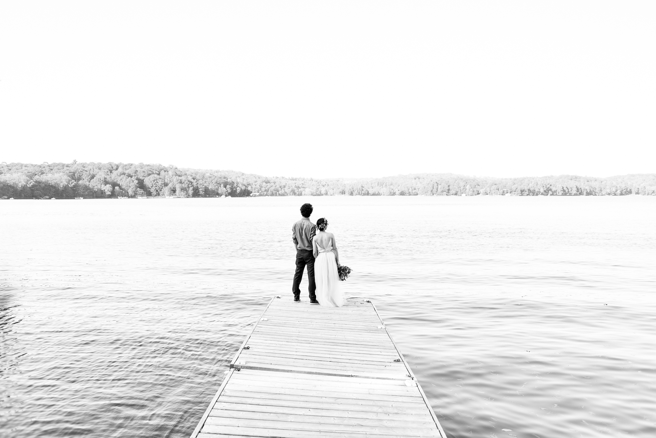 Black and white wedding photo of a couple on a dock on the lake 