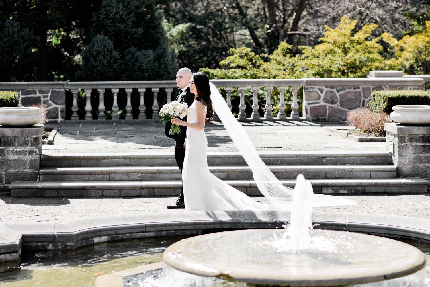 Bride and Groom walk around the fountain in the gardens of Graydon Hall