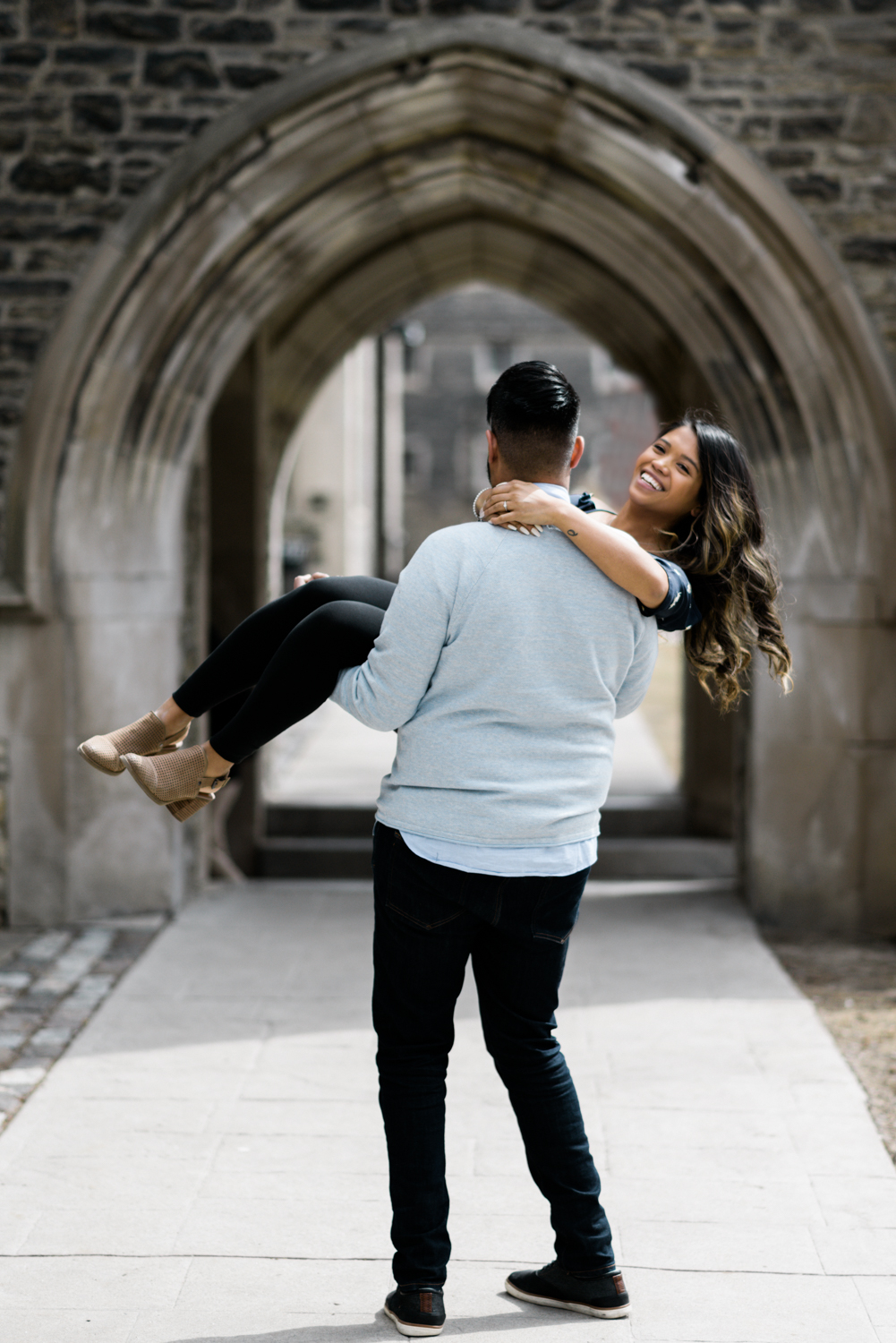 Man holding bride in his arms and swinging around at the arch at Victoria College, Toronto photographed by Alix Gould