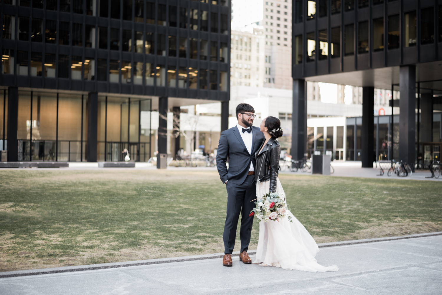 Bride in leather jacket with groom in blue suit at TD tower in downtown Toronto