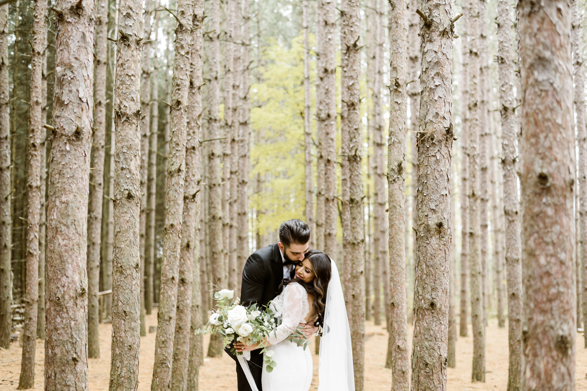 Bride and groom kiss in a pine grove near Chateau le Parc