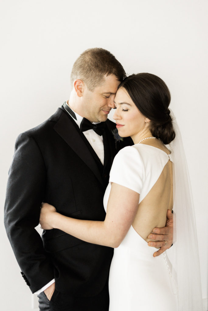 Classic, simple bride and groom wedding photo against white wall